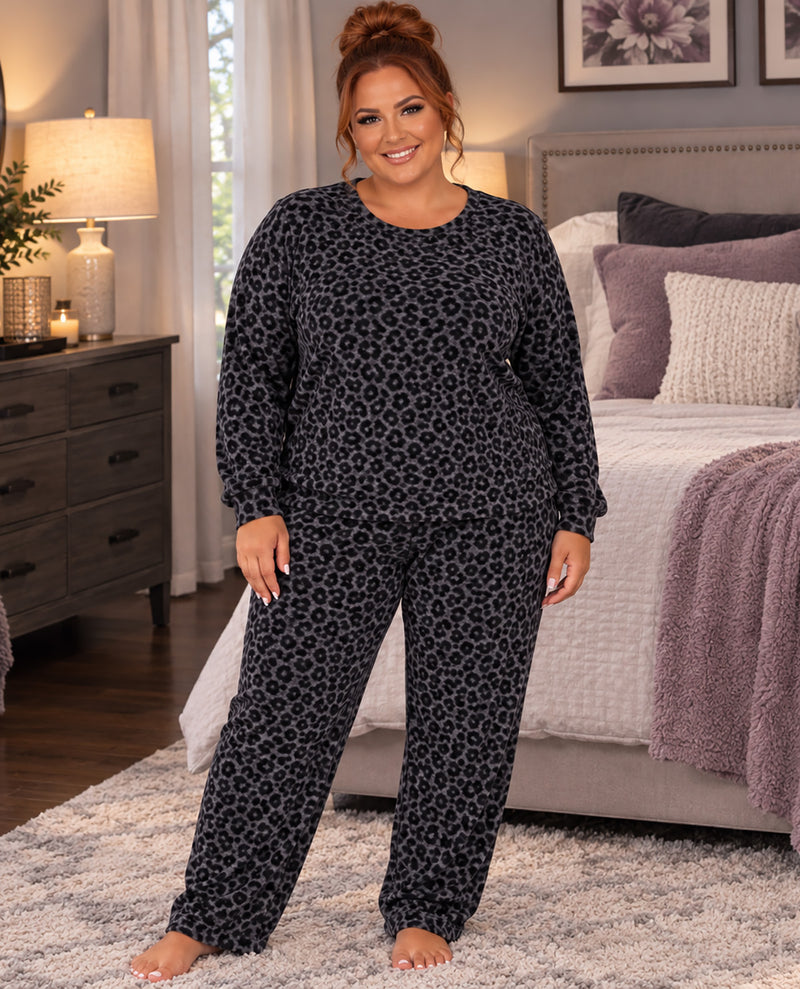 A woman modeling a matching two-piece pajama set with a dark gray and black leopard print, standing in a bedroom setting.