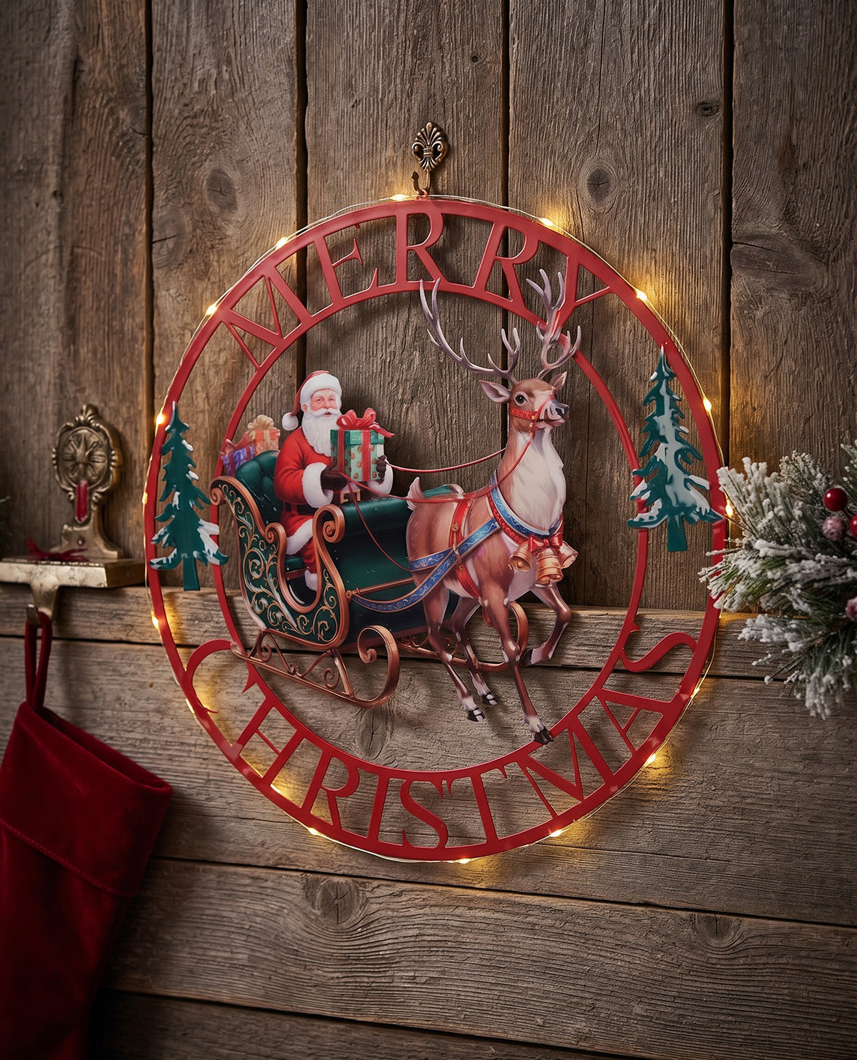A festive round metal Christmas wall sign featuring Santa Claus in a sleigh pulled by a reindeer, with the words “MERRY CHRISTMAS” in red cutout lettering. The sign is lit with warm white string lights and displayed against a rustic wooden wall, with a red stocking and holiday greenery nearby.