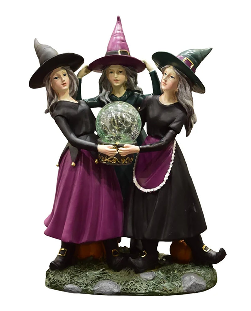 Three witch figurines standing together on a decorative base, each wearing a pointed hat and long dark dress, holding a glowing crystal ball. The scene is isolated on a plain white background.