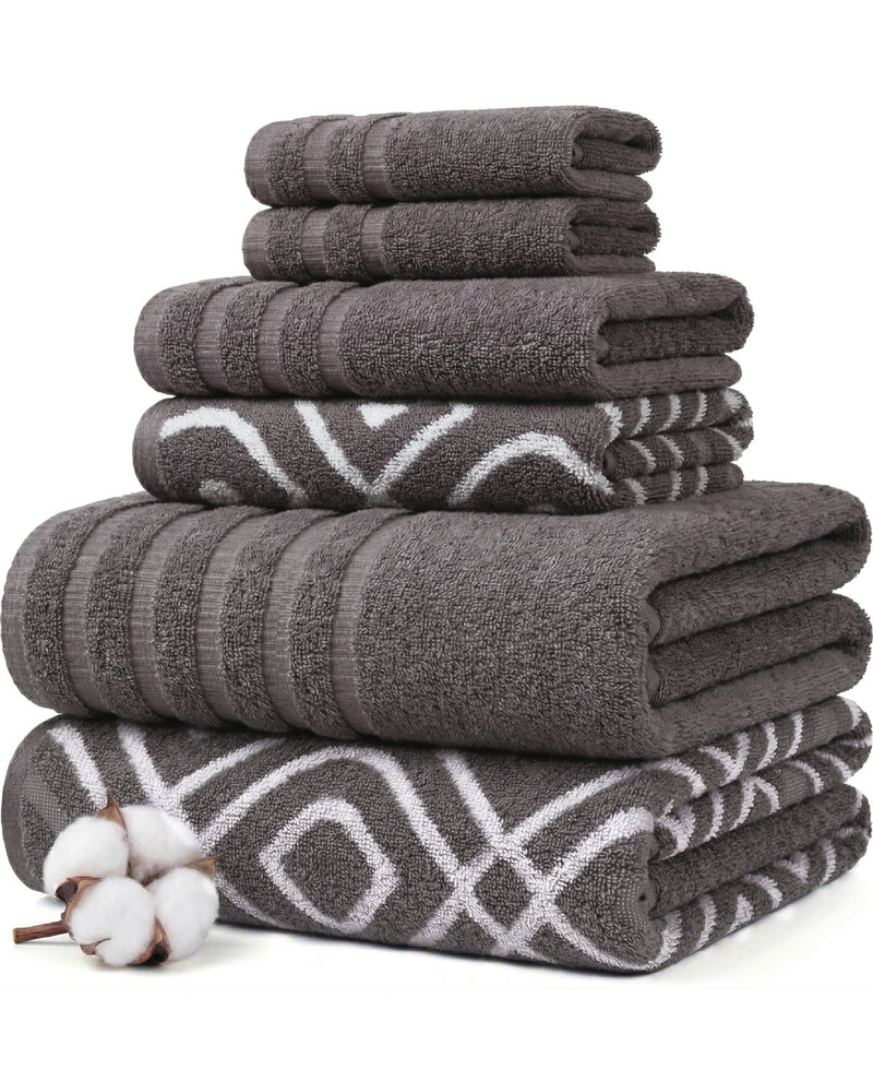 A stack of folded bath towels in dark gray and charcoal tones, including solid textured towels and patterned towels with white geometric designs. A small cotton boll is placed in the lower left corner on a clean white background.