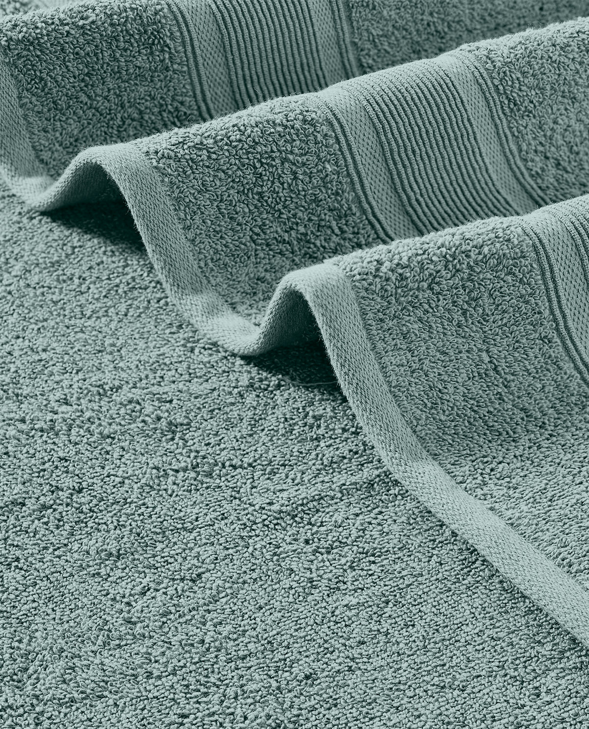 A close-up of a folded bath towel in a muted sage green color, showing the textured terry cloth body and ribbed border.