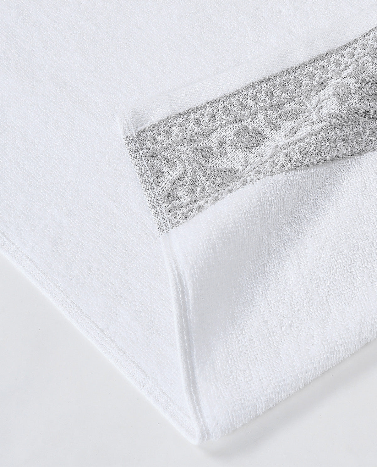 A close-up of a white folded towel featuring a decorative gray embroidered border along the fold.