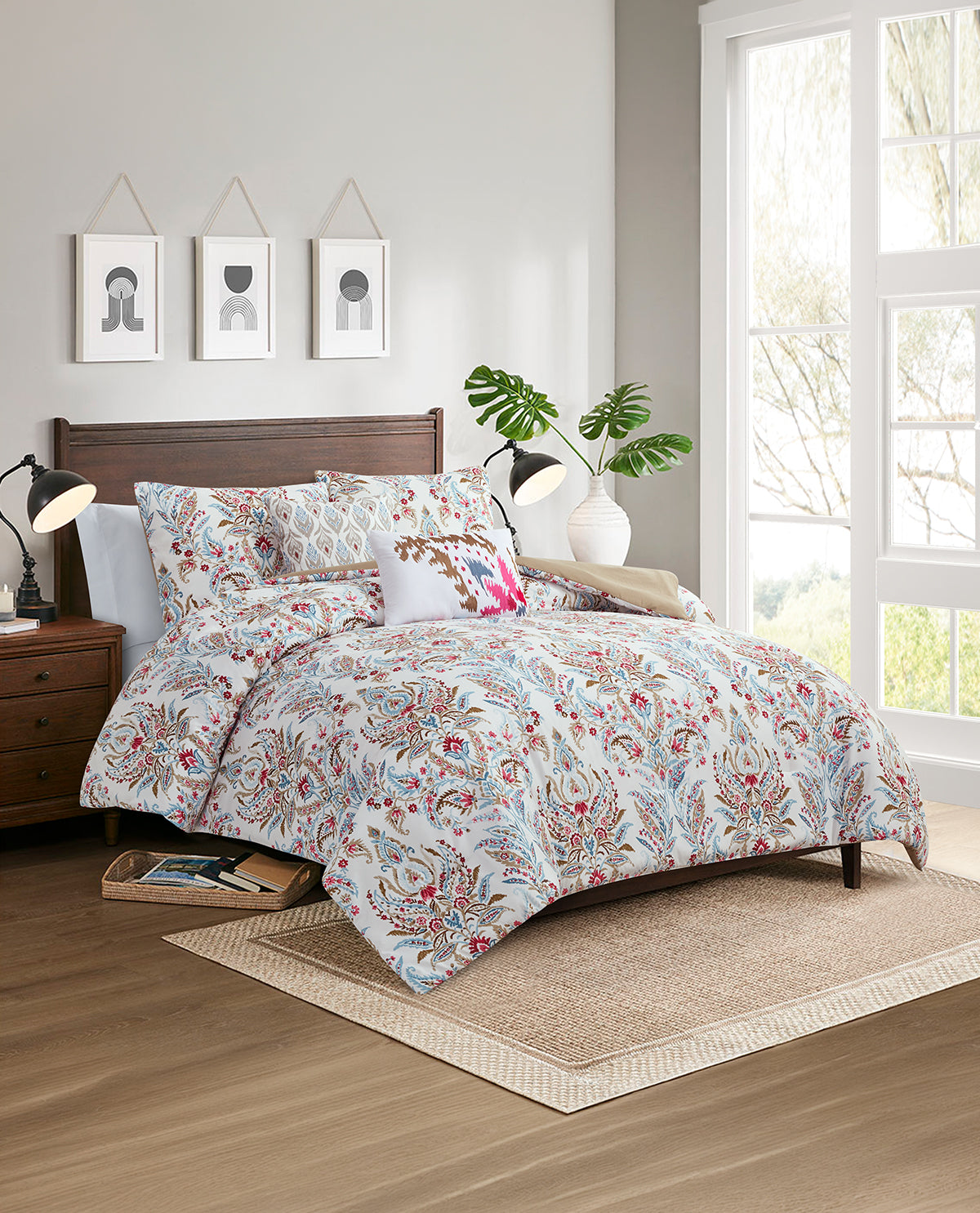 A bed dressed in a light blue and red botanical patterned comforter set with matching pillows, styled in a bright, modern bedroom with a wooden headboard, bedside lamps, and a window.