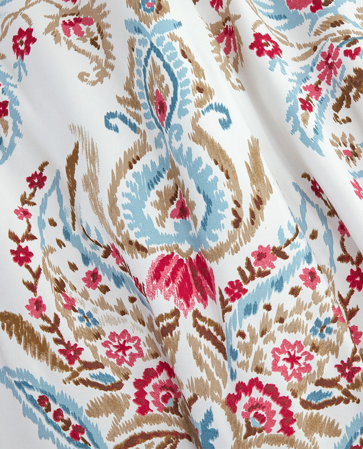 A close-up of a draped fabric with an intricate pattern featuring light blue, brown, and bright pink floral motifs on a white background.