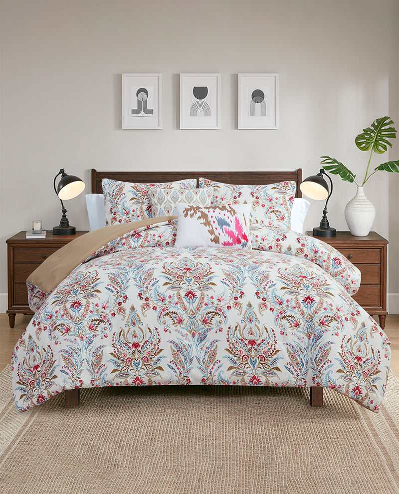 A bed dressed in a white comforter and matching pillow shams with an intricate multicolor floral and ornamental pattern, styled in a modern bedroom setting with wooden nightstands, lamps, and wall art.