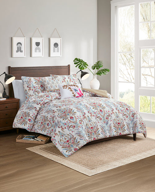 A bed dressed in a light blue and red botanical patterned comforter set with matching pillows, styled in a bright, modern bedroom with a wooden headboard, bedside lamps, and a window.