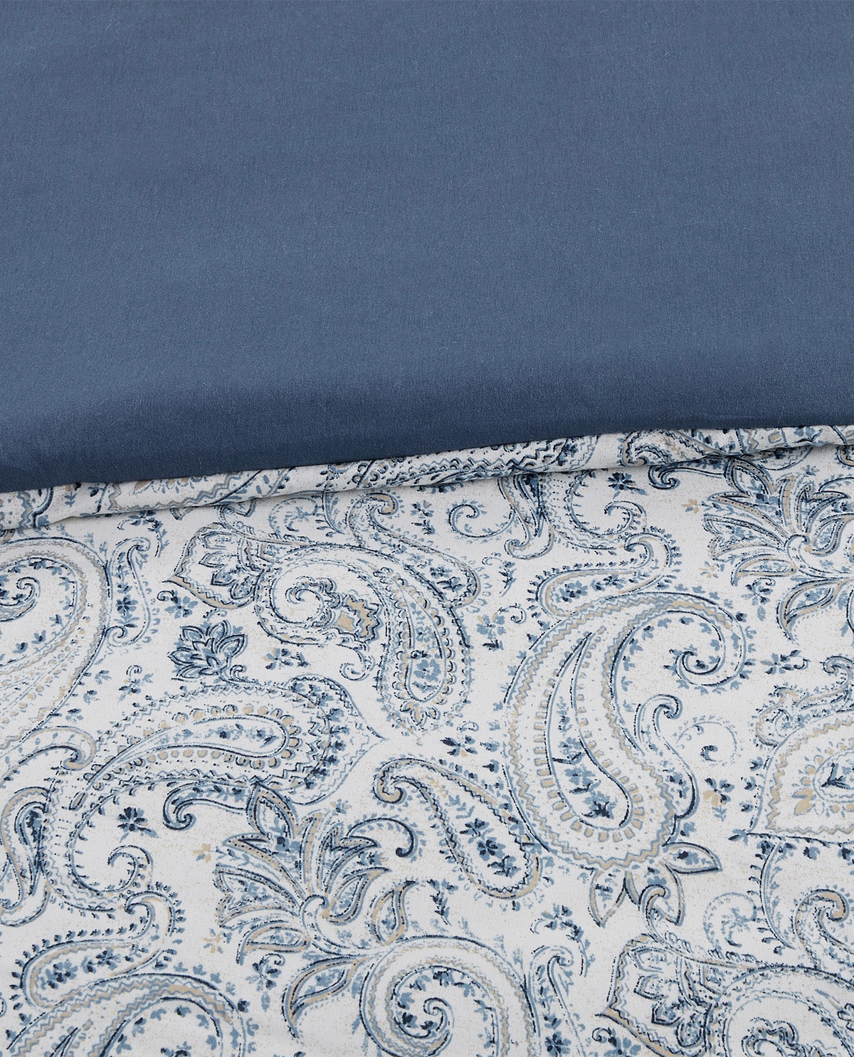 A close-up of a folded textile showing a solid slate blue top section and a white bottom section with an intricate blue paisley pattern.