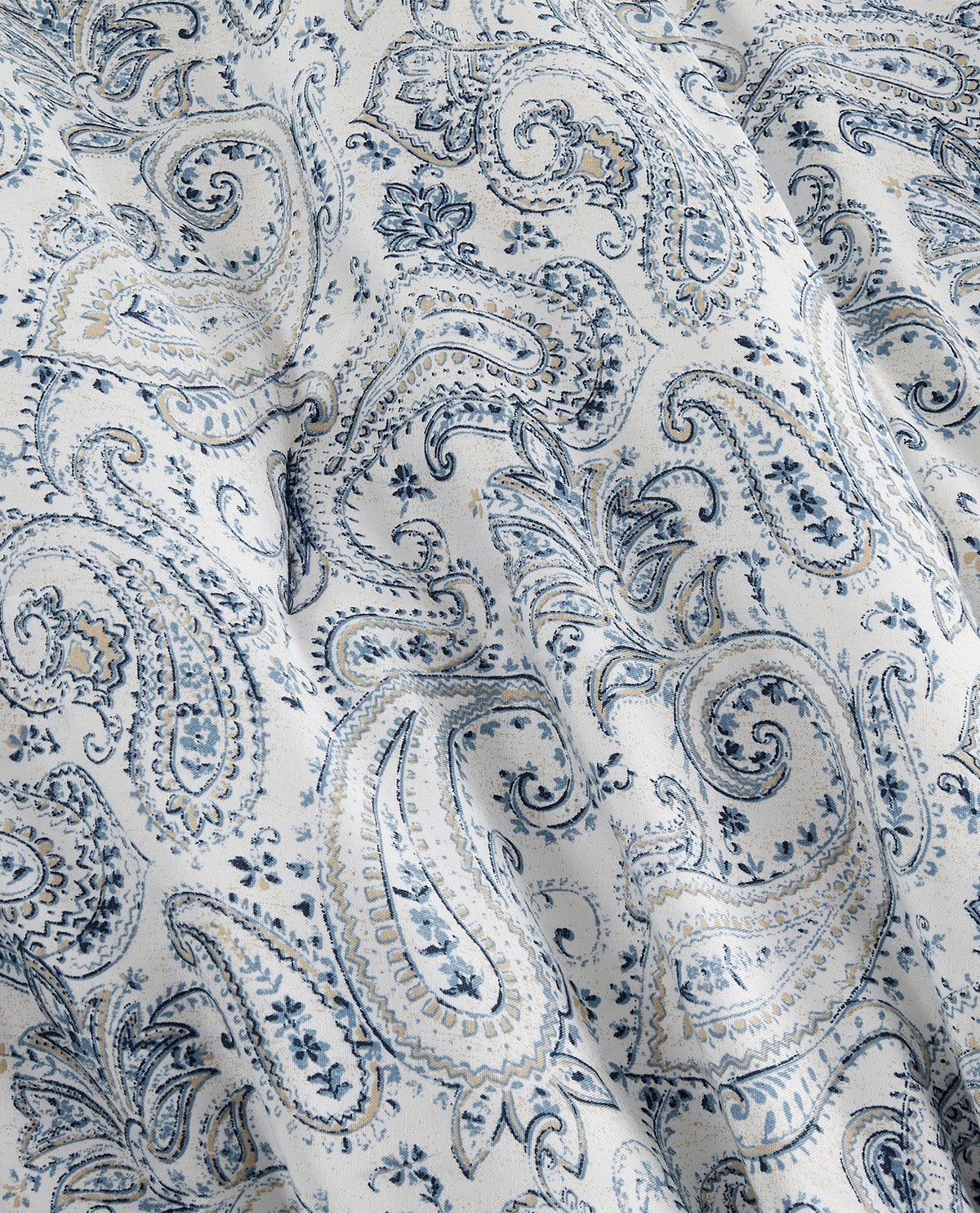A close-up of draped fabric featuring a classic blue and gray paisley pattern on a white background.