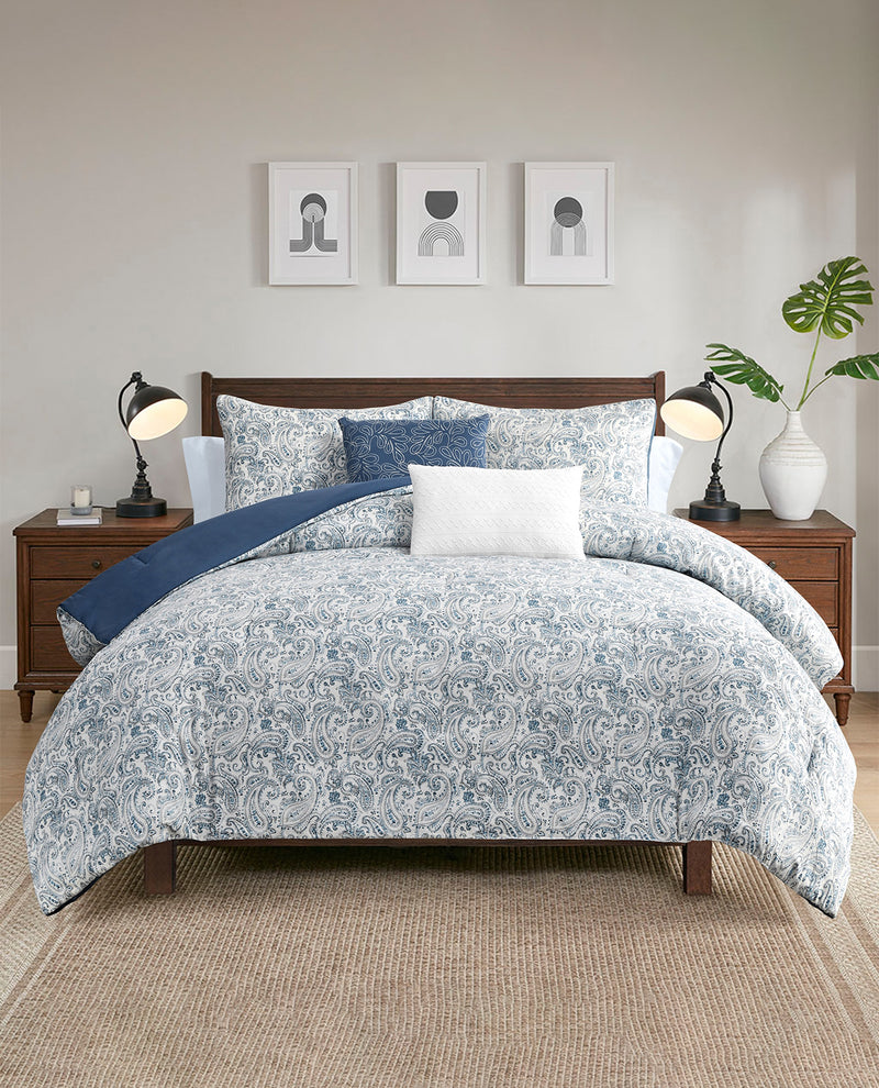 A neatly made bed in a styled bedroom setting, featuring a light blue and white floral patterned comforter set with matching pillows and a white accent pillow. The bed is flanked by matching wooden nightstands with black table lamps, and the wall behind is decorated with three minimalist framed prints.