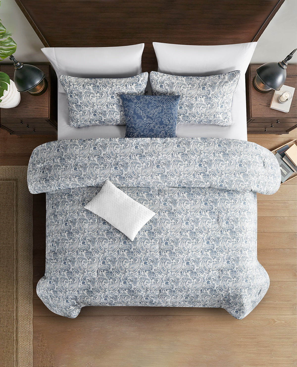A top-down view of a neatly made bed with a light blue and white floral patterned comforter, matching pillow shams, a floral-print blue accent pillow, and white pillows, set against a dark wood headboard and bedside tables.