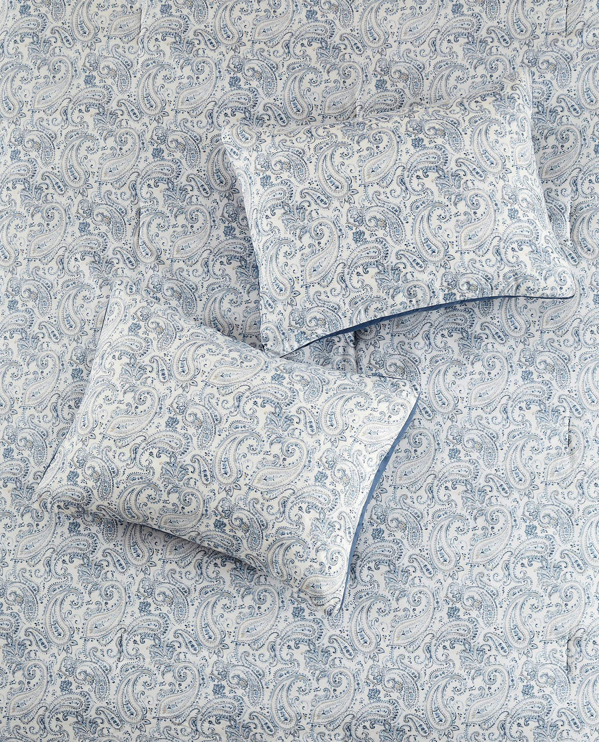 A close-up of a bedding set featuring a light blue and white paisley pattern on the comforter and two matching pillowcases.