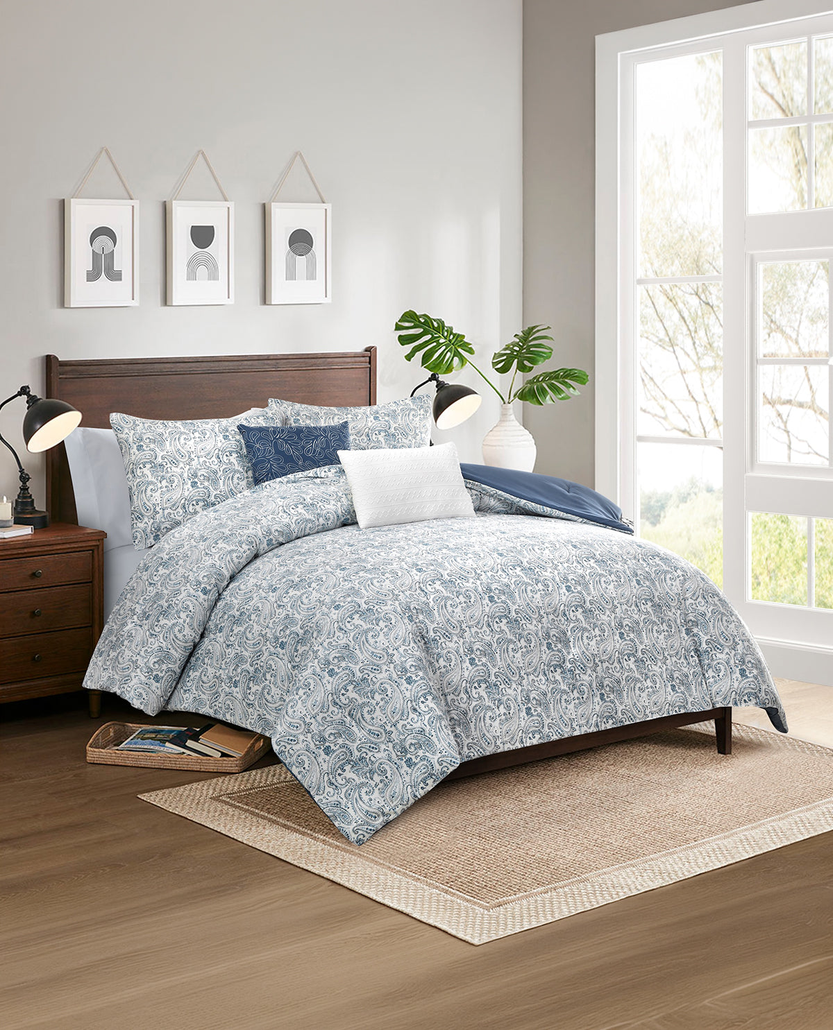 A bed dressed in a light blue and white floral patterned comforter set with matching pillows, styled in a bright bedroom with a wooden headboard, nightstand, window, and rug.