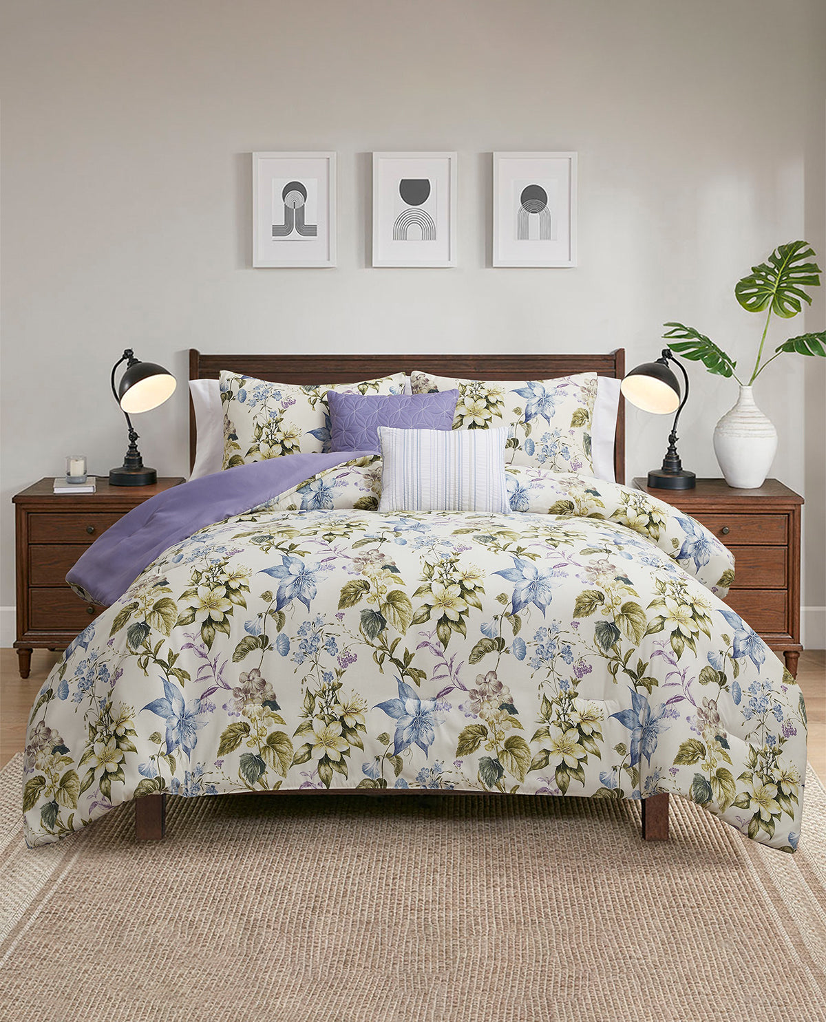 A floral comforter set styled on a bed in a modern bedroom. The comforter features a cream background with a blue, green, and purple botanical pattern, accompanied by patterned purple and white accent pillows.