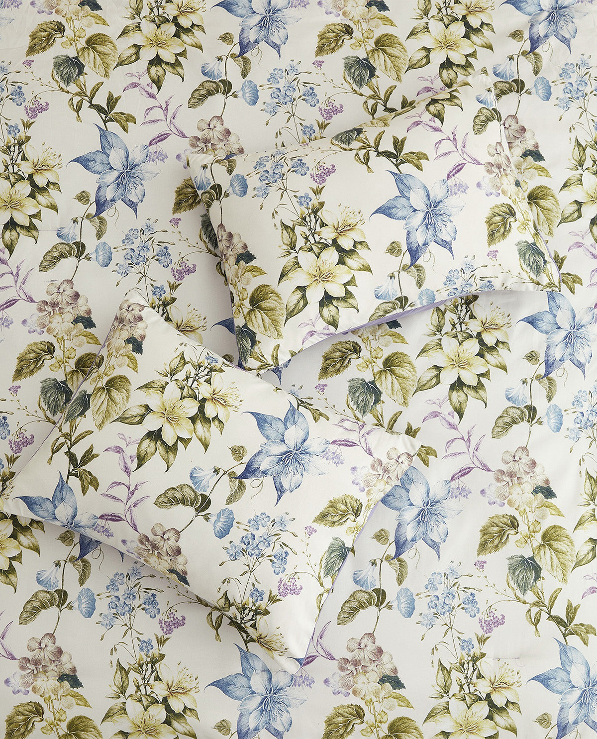 Two decorative pillows with a vintage floral print, arranged on top of a matching floral fabric background. The print features blue, purple, and green flowers on an off-white base.