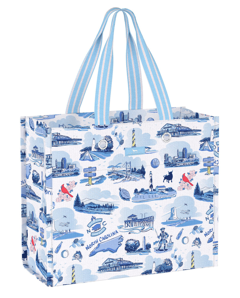 A reusable tote bag with a blue and white illustrated pattern of North Carolina landmarks, featuring light blue and white striped handles, shown on a solid white background.