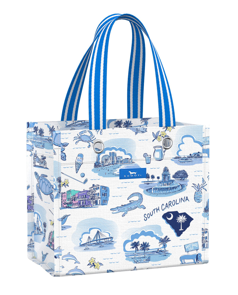A white tote bag featuring a blue 'South Carolina' coastal-themed toile-style print with illustrations of crabs, sea turtles, sailboats, and buildings, complete with blue and white striped handles.