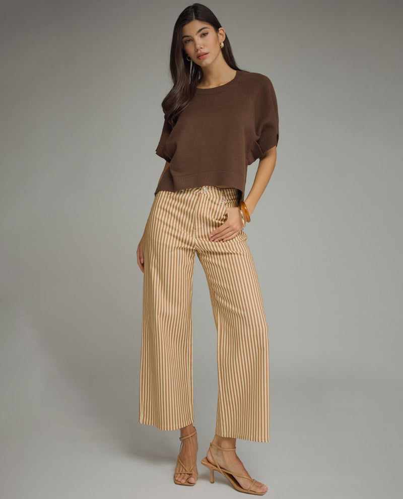 A model stands against a neutral gray studio background wearing a brown short-sleeve knit top, beige wide-leg cropped pants with thin vertical stripes, and nude high-heeled sandals.