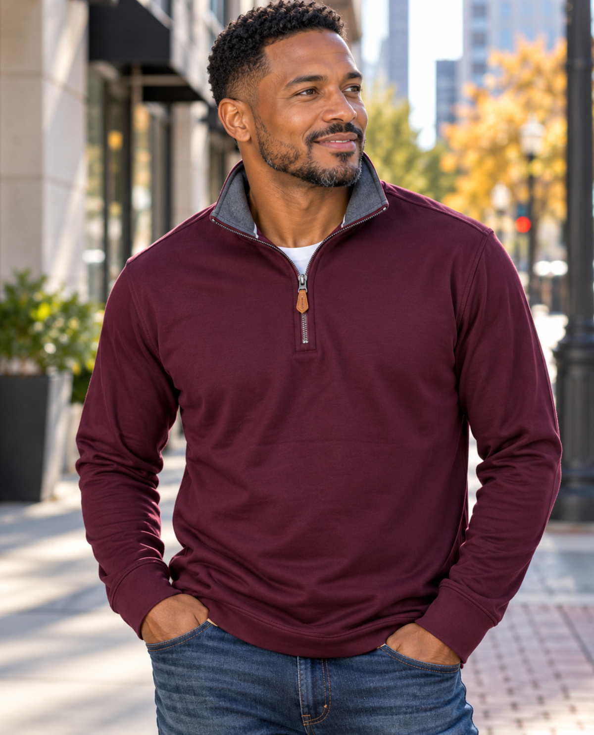 A man wearing a burgundy quarter-zip pullover sweater with a gray mock neck collar, standing outdoors on a city sidewalk.
