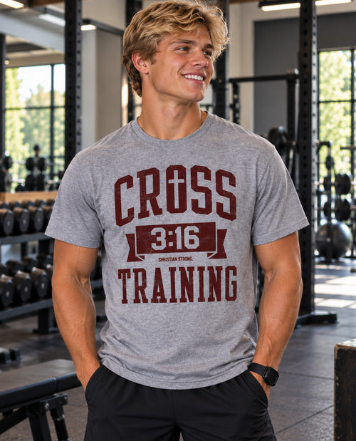 A smiling man in a gym wearing a heather gray t-shirt with a dark red graphic that reads 'CROSS 3:16 TRAINING' and 'CHRISTIAN STRENGTH'.