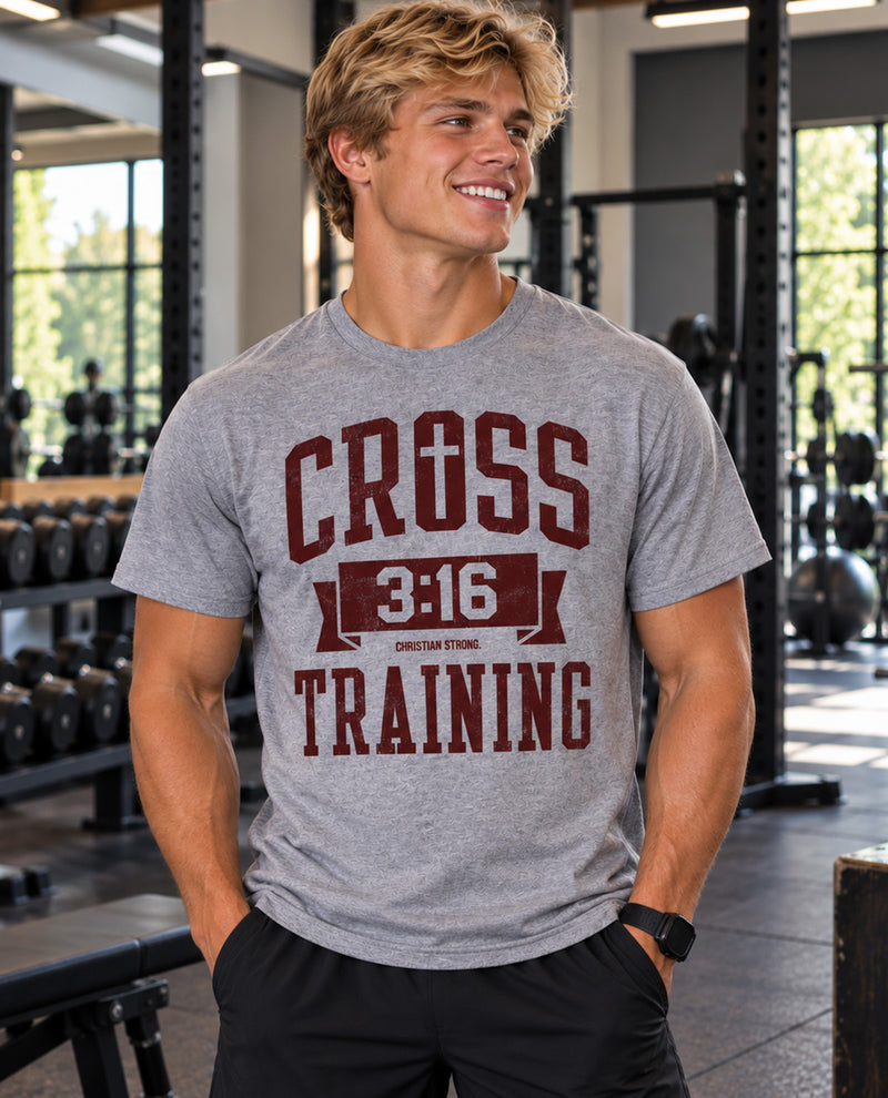 A smiling man in a gym wearing a heather gray t-shirt with a dark red graphic that reads 'CROSS 3:16 TRAINING' and 'CHRISTIAN STRENGTH'.