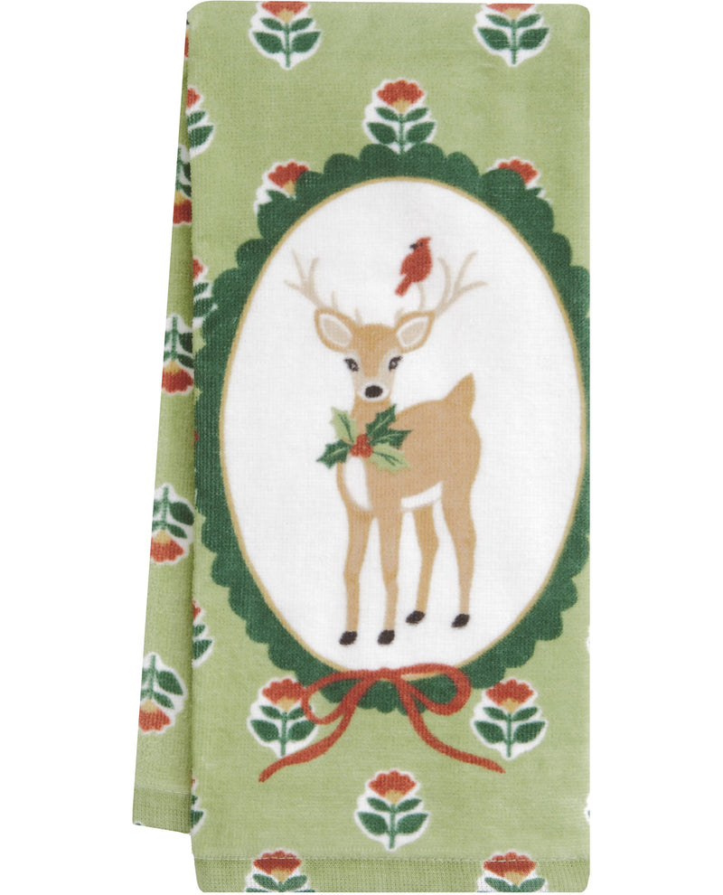 A folded decorative towel or cloth featuring a central oval design with a tan deer, green holly leaves, a red bird, and a red ribbon, set on a light green floral background.