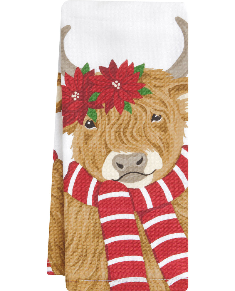 A folded white kitchen towel featuring a printed illustration of a Highland cow wearing a red poinsettia flower crown and a red-and-white striped scarf.