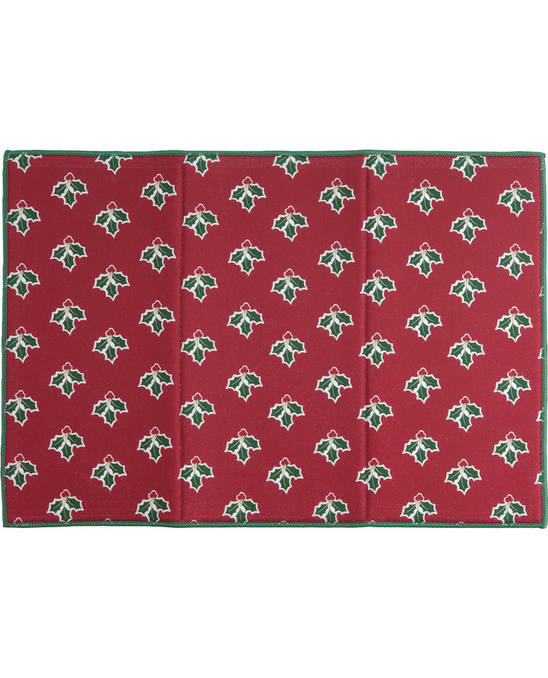 A rectangular red fabric item, likely a blanket or mat, featuring a repeating green holly leaf and red bow pattern with a solid green border, shown flat against a white background.