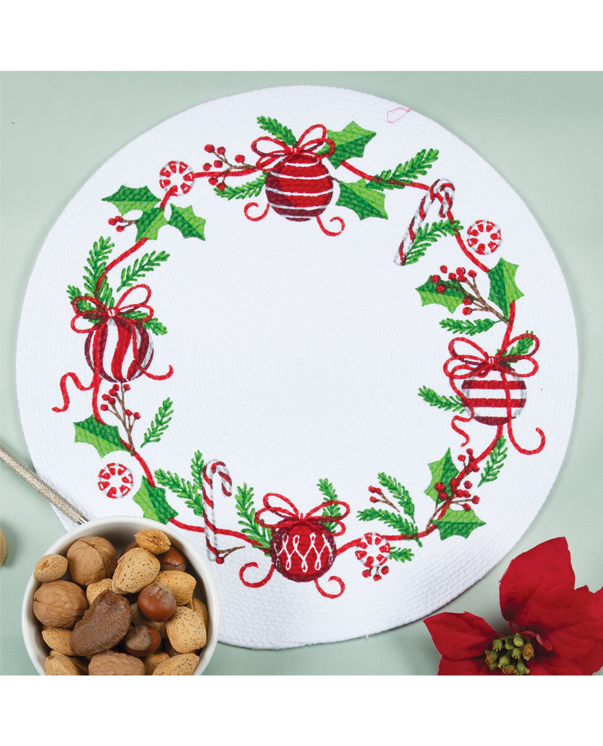 Decorative plate with Christmas design, surrounded by a bowl of nuts and a poinsettia flower.