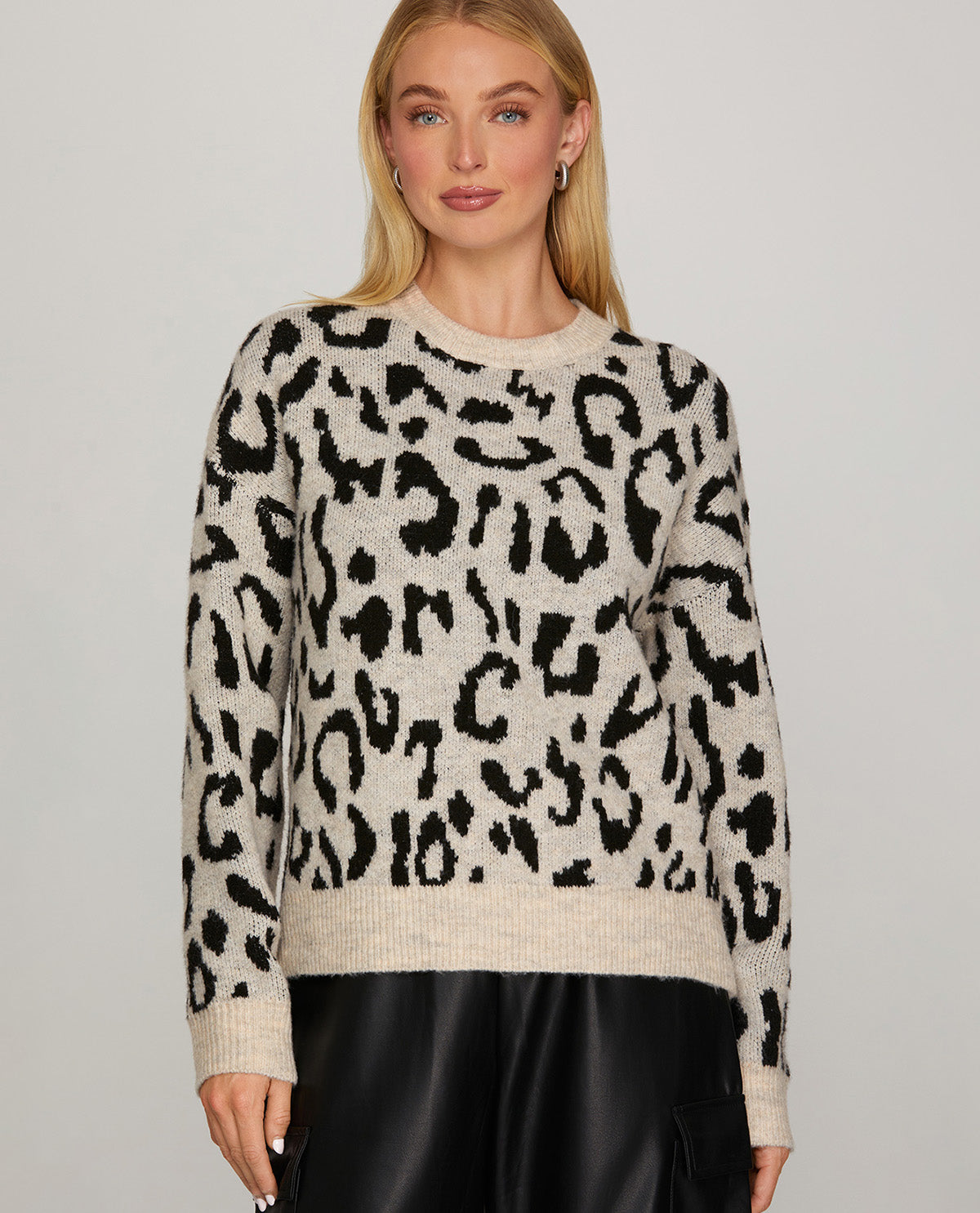 A woman wearing a fuzzy knit crewneck sweater with a black leopard print on a warm beige background, paired with black pants, against a light gray studio background.