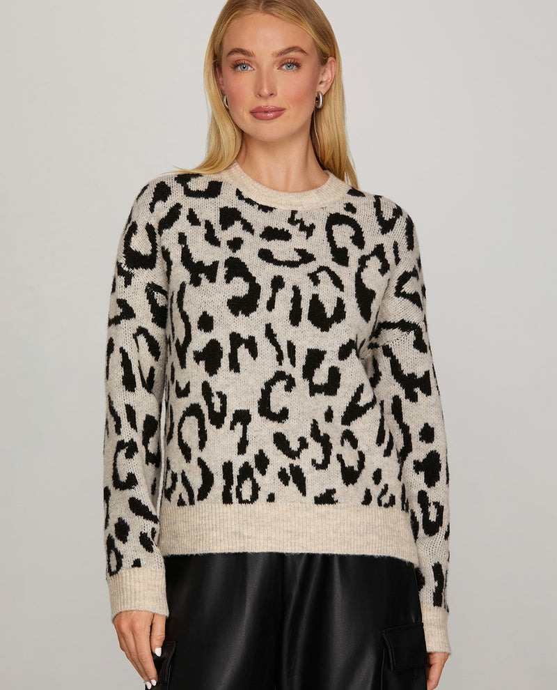 A woman wearing a fuzzy knit crewneck sweater with a black leopard print on a warm beige background, paired with black pants, against a light gray studio background.