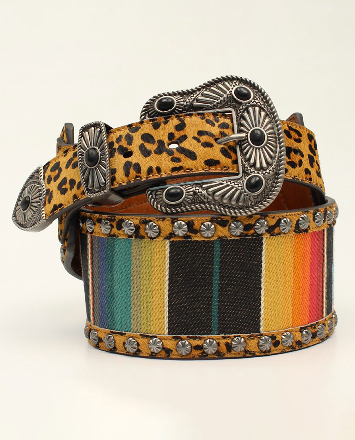 A western-style belt with a leopard print strap, a multicolor rainbow stripe section, silver-tone studs, and ornate silver concho buckles, shown coiled on a light beige background.