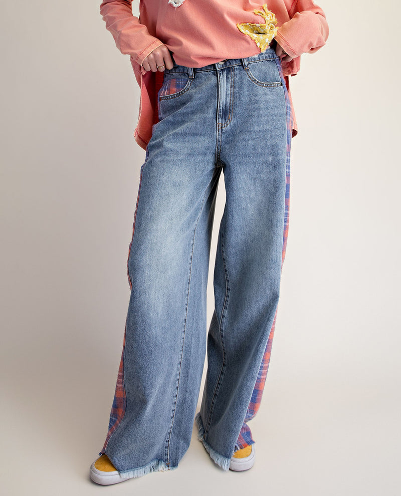 A person wearing light blue wide-leg denim jeans with red and blue plaid side panels, styled with a pink top and yellow sneakers against a plain light beige studio background.