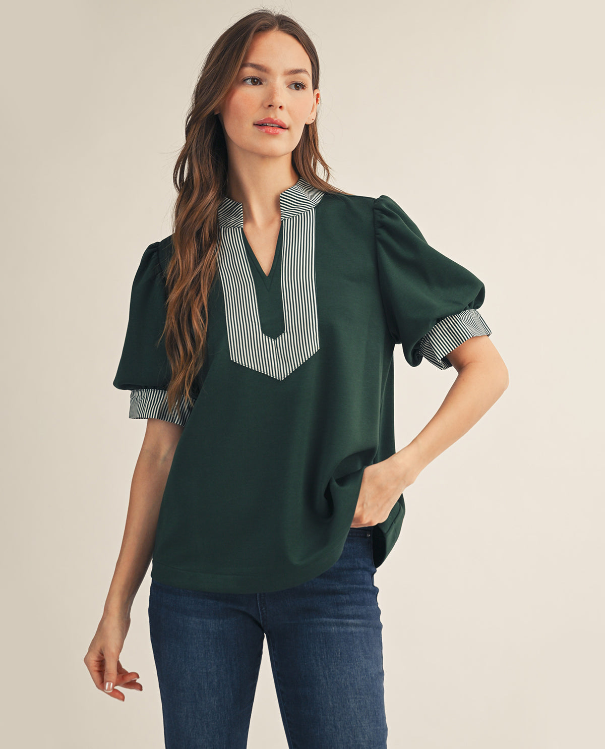 Woman wearing a green blouse with striped collar against a beige background