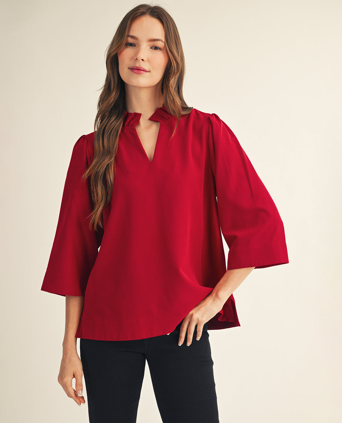 A woman modeling a vibrant red three-quarter sleeve blouse with a split V-neckline, paired with black pants, against a solid light beige background.