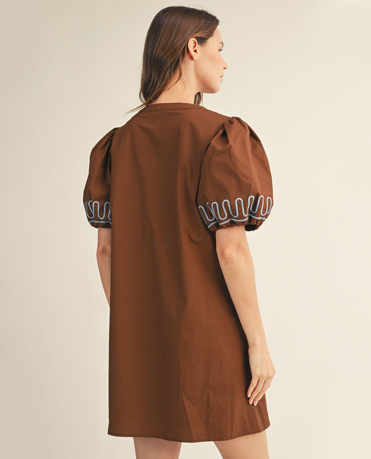 Woman wearing a brown dress with embroidered sleeves on a beige background