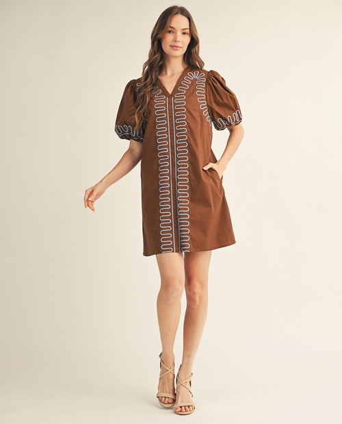 Woman wearing a brown dress with embroidery on a beige background