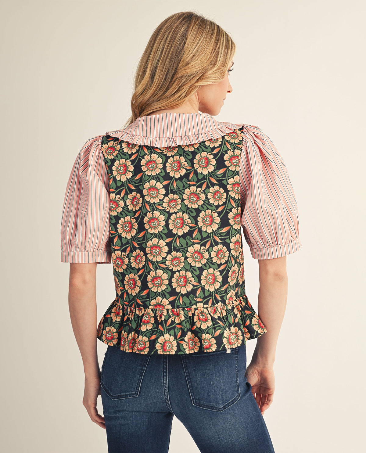 Woman wearing a floral vest over a striped shirt with a beige background