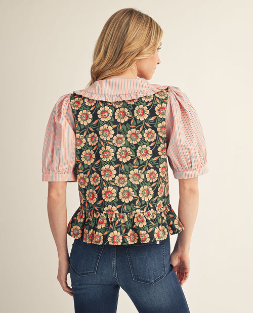 Woman wearing a floral vest over a striped shirt with a beige background