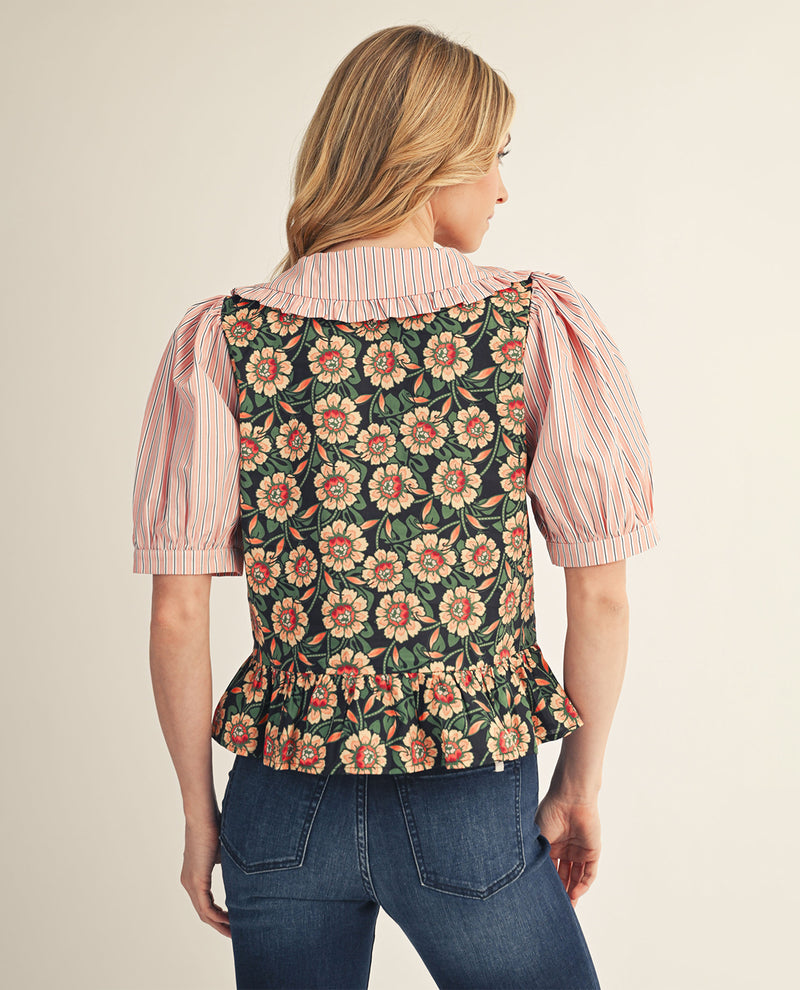 Woman wearing a floral vest over a striped shirt with a beige background