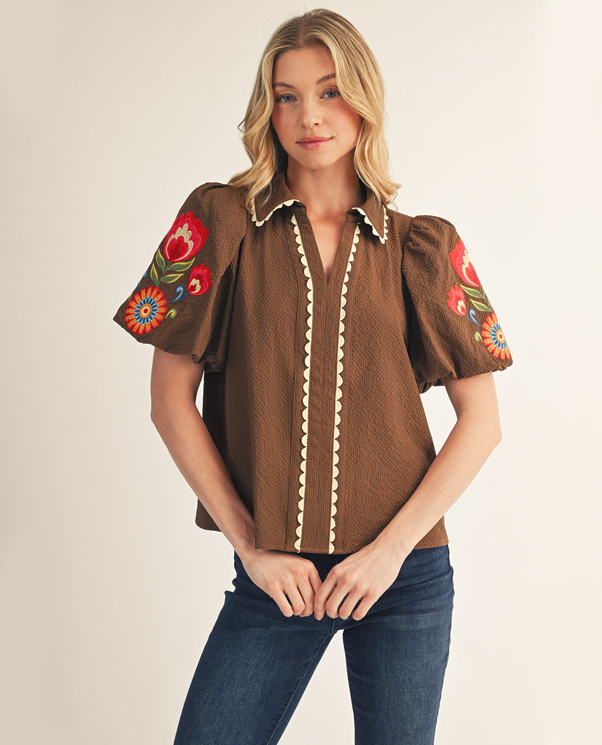 Woman wearing a brown blouse with floral embroidery on a plain background