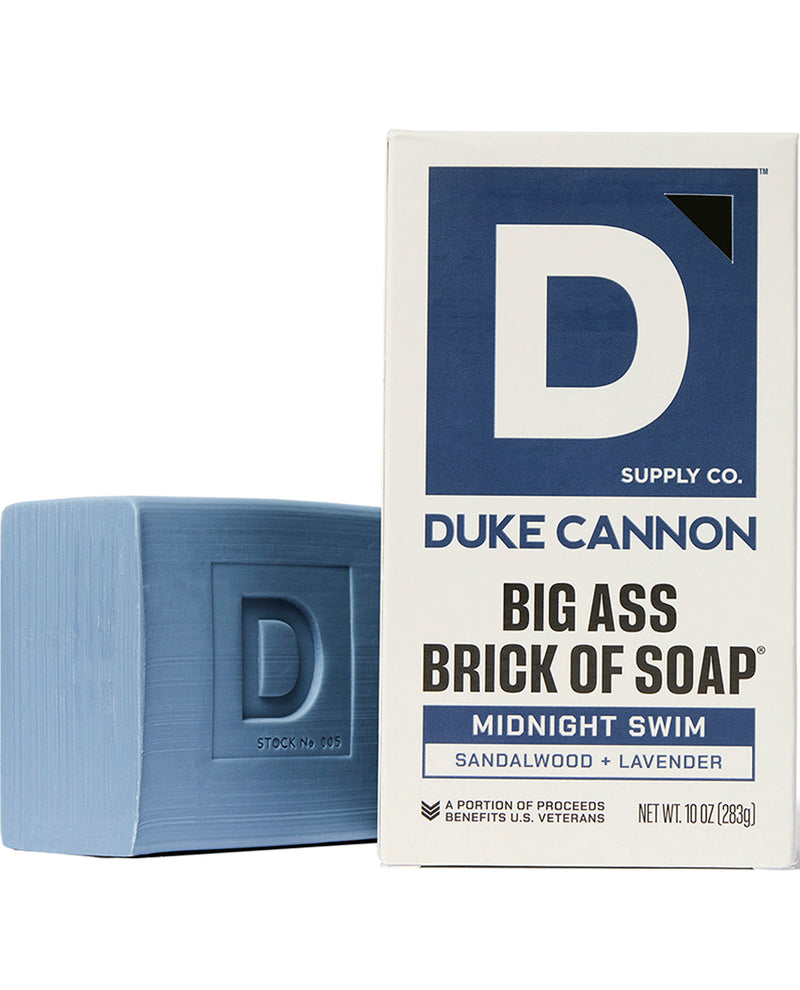 A bar of Duke Cannon Big Ass Brick of Soap in the Midnight Swim scent, shown next to its white and navy blue retail box on a clean white background.