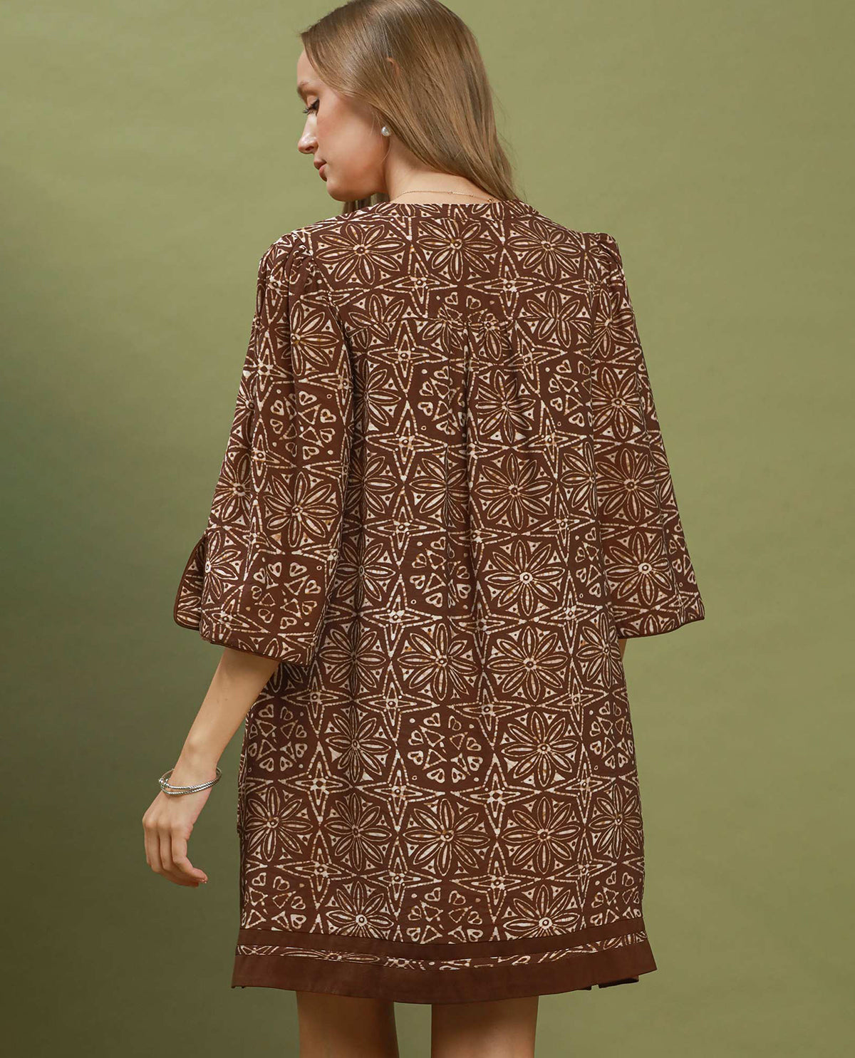 Woman wearing a brown patterned dress against a green background