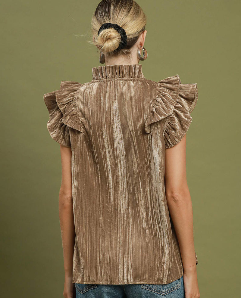 A woman viewed from the back wearing a taupe-brown ruffled velvet blouse with a high ruffled collar, set against a solid olive green background.