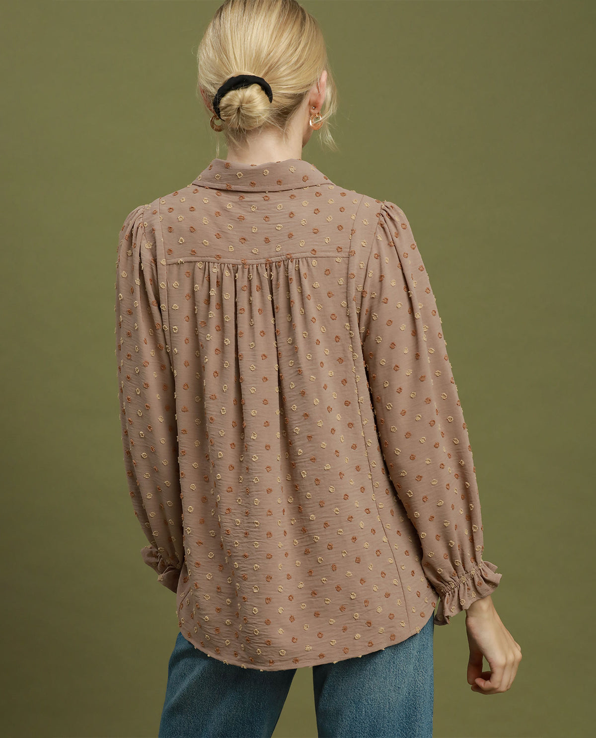 A woman shown from the back wearing a long-sleeve blouse with a brown and beige micro-pattern, paired with blue jeans, against a solid olive green background.