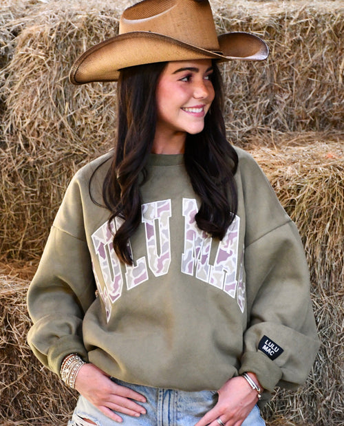 Woman wearing a green sweatshirt with 'LULU' printed on it, standing in front of hay bales.