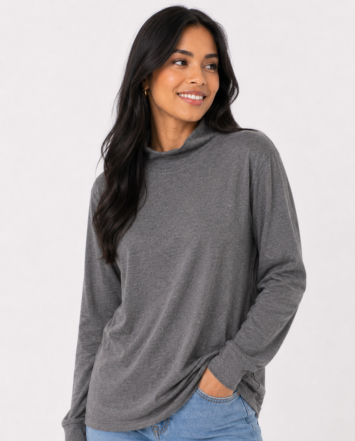 A woman wearing a dark gray long-sleeve mock neck top and light blue jeans, standing against a plain white studio background.