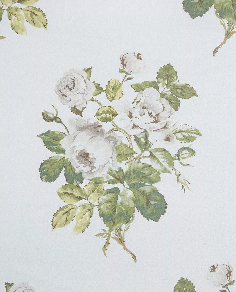 A close-up of a floral print featuring white roses with green leaves on a very light off-white background.