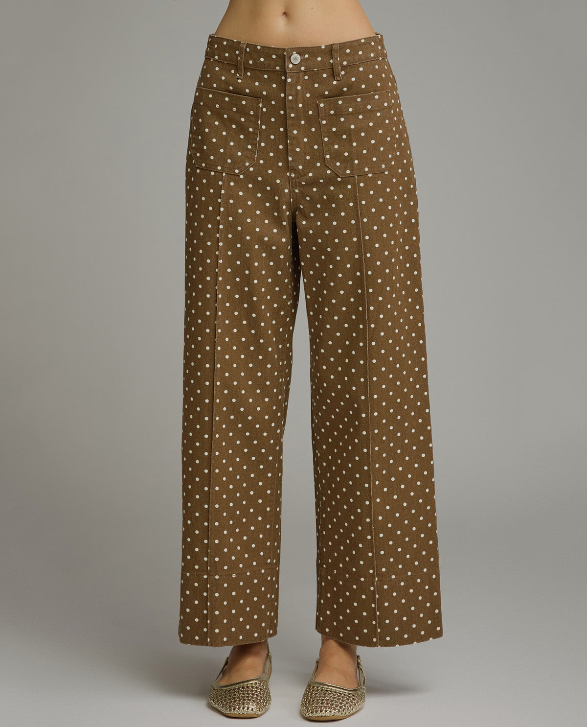 Model wearing brown straight fit polka dot pants with a gray background