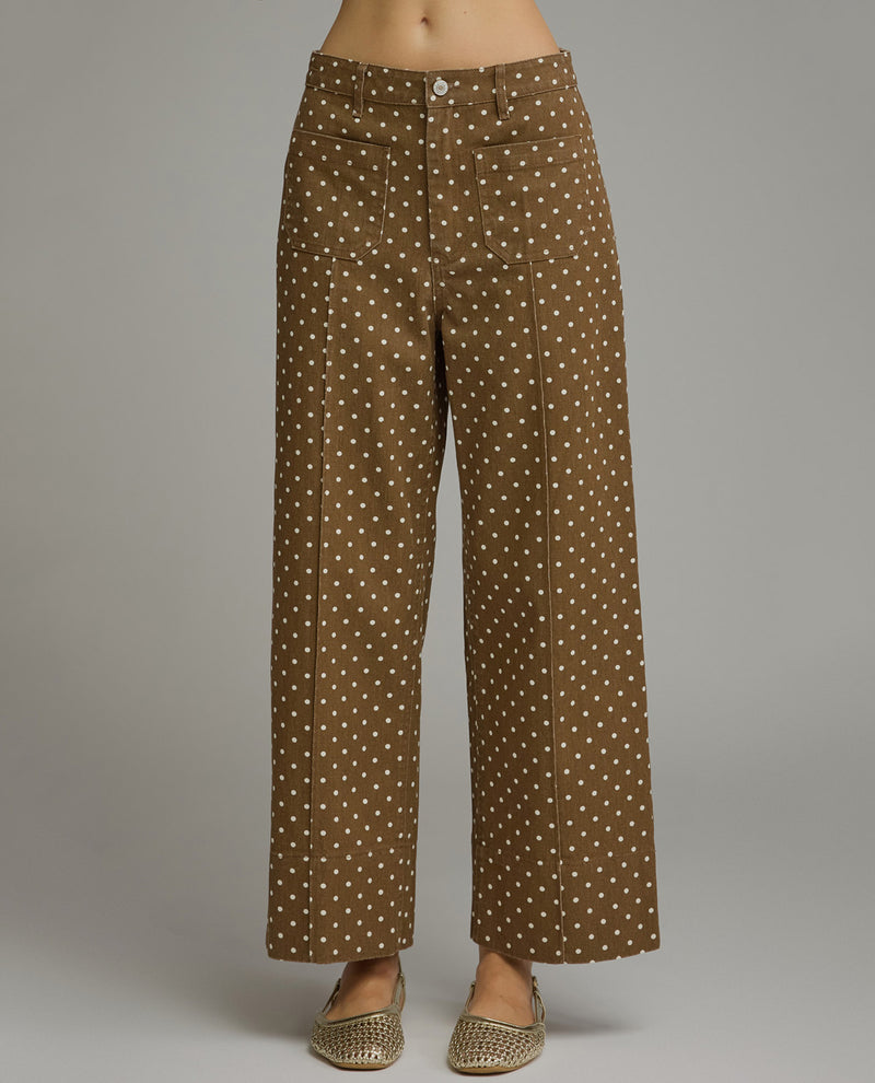 Model wearing brown straight fit polka dot pants with a gray background
