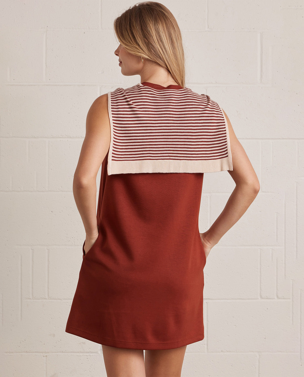 Woman wearing a red and white striped dress against a light tiled wall.